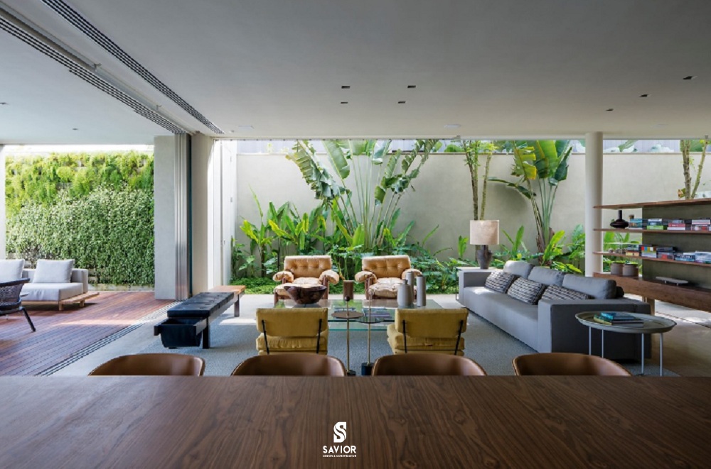 Phòng khách sang trọng với tầm nhìn mát mắt ra sân vườn nơi hông nhà. Cặp ghế bành tông vàng đồng nổi bật trên nền xanh lá cây.